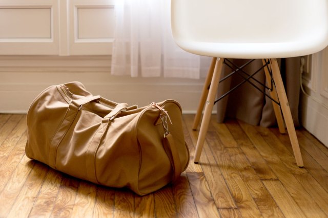 An image of a brown duffel bag beside a white and brown wooden chair