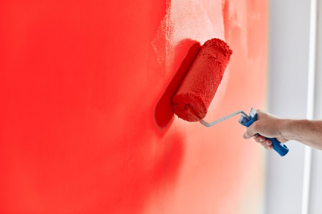 A person uses a paint roller to paint a wall red