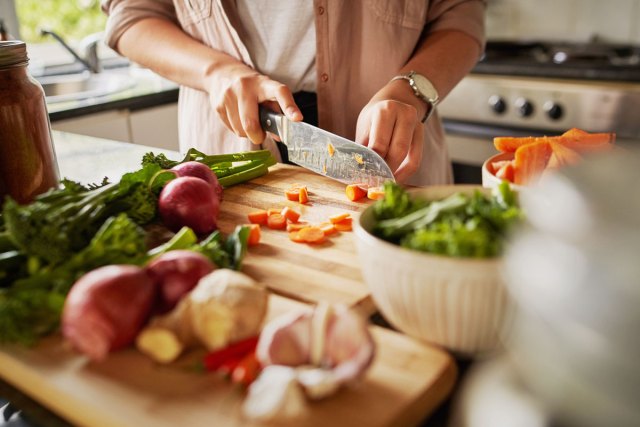 An image of a woman cutting vegetables on a wooden cutting board in a kitch