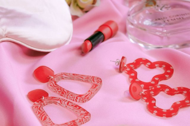 An image of red lipstick and red jewelry on pink fabric