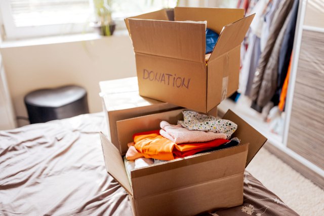 An image of two cardboard boxes filled with clothes on a bed with a closet in the background