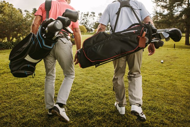 An image of two men walking on a golf course with golf bags
