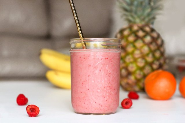 An image of a pink smoothie with various fruit in the background