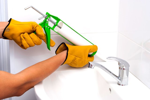 An image of a person wearing yellow gloves using a caulking gun on a sink
