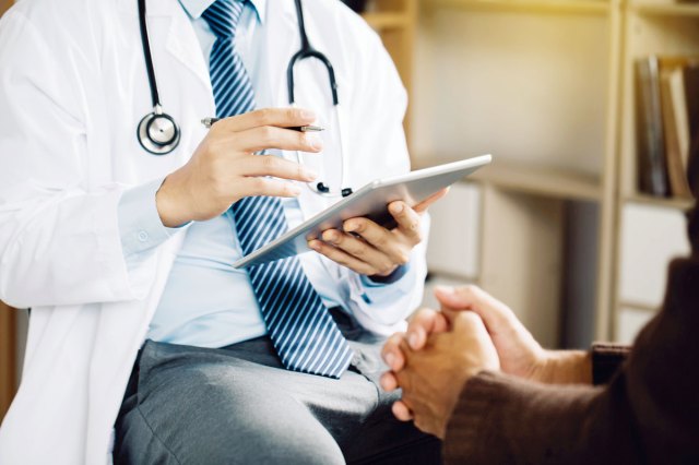 A doctor wearing a white coat and stethoscope talks to a person