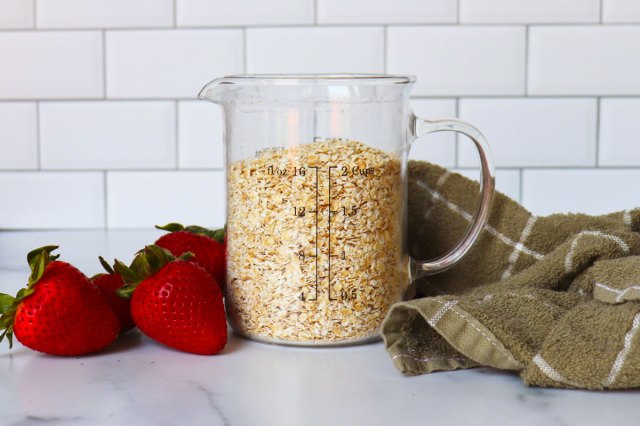 An image of strawberries on a counter beside clear glass pitcher filled with oats