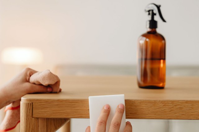 An image of hands cleaning a wooden table with a white sponge and rag