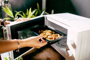 A woman puts food into the microwave