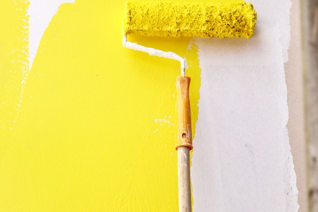 A roller brush painting a white wall yellow