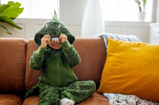 An image of a little boy in a dinosaur costume sitting on the couch