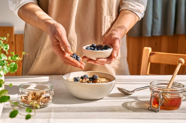 An image of a woman putting blueberries in the bowl with oatmeal 