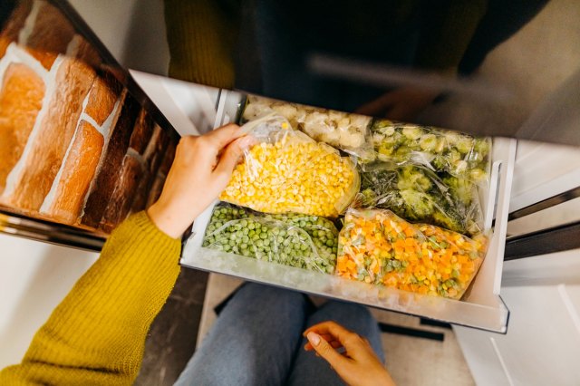 An image of a person taking a bag of corn out of a freezer filled with other bags of vegetables
