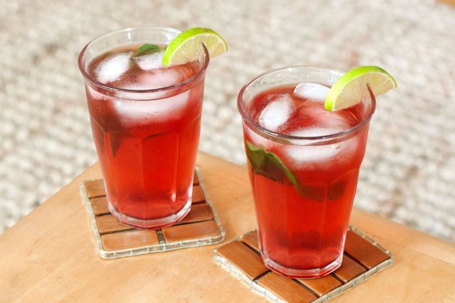An image of two red drinks with limes on a wooden table