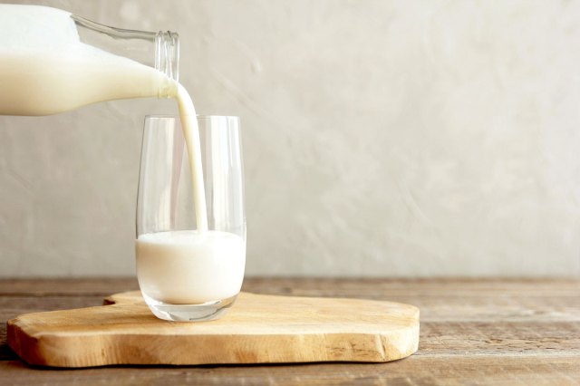 An image of a glass of milk being poured from a glass bottle on a wooden cutting board