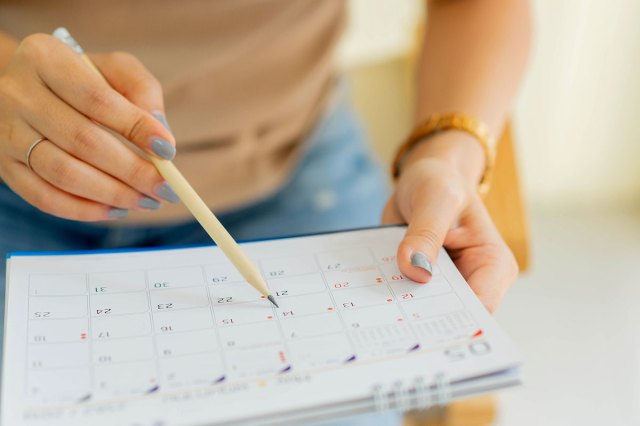 A woman makes notes on a paper calendar with a pencil