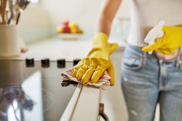 An image of person wearing yellow rubber gloves cleaning a stove