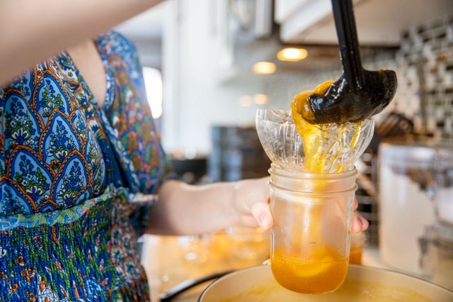 An image of a woman ladling orange jam into a jar