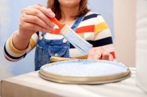 A woman wearing a striped shirt and overalls puts paint on a paintbrush
