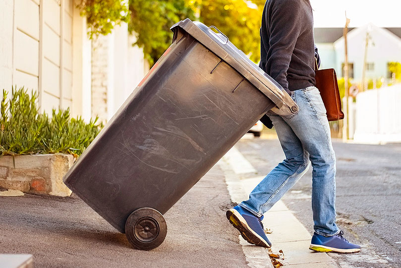 An image of a man rolling a trash can down a driveway