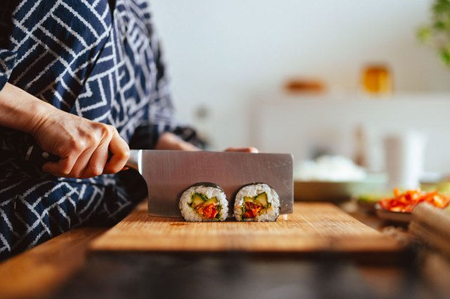 An image of a person cutting a sushi roll on a wooden cutting board
