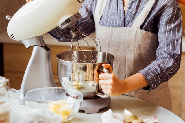 An image of hands of a woman in an apron using a stand mixer at home.