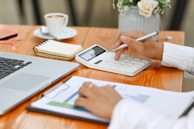 An image of a businesswoman using calculator and analyzing financial document on wooden desk