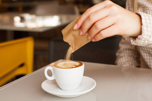 An image of a woman pouring a packet of sugar into a cup of coffee