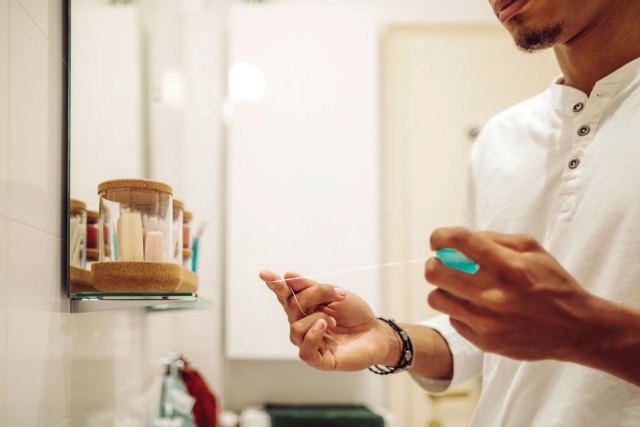 An image of a man in a bathroom taking floss out of a container