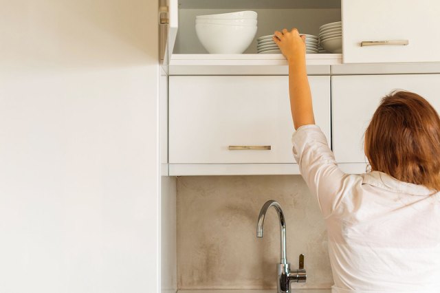 An image of a woman getting a dish from a kitchen cabinet