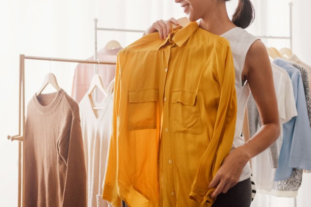 An image of a woman holding a shirt on a hanger up to her body