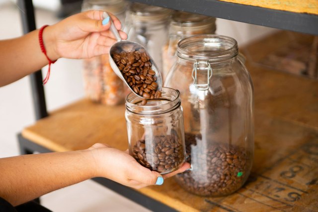 An image of hands serving bulk coffee beans into a reusable glass container 