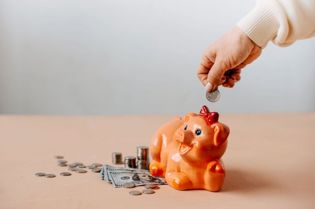 An image of a person putting a coin into an orange piggy bank surrounded by money