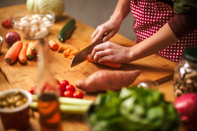 An image of a woman chopping vegetables on a wooden cutting board