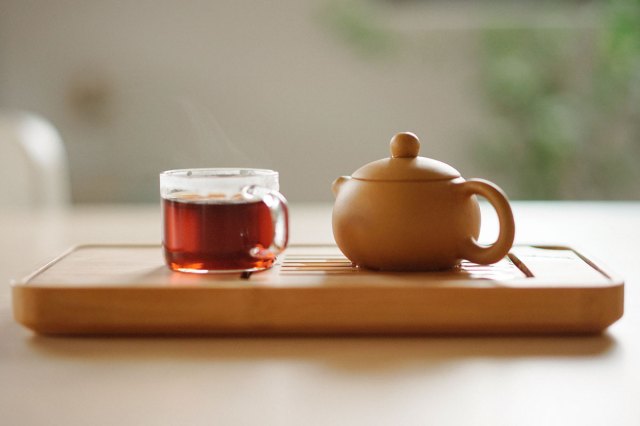 An image of a clear glass cup with tea near brown ceramic teapot