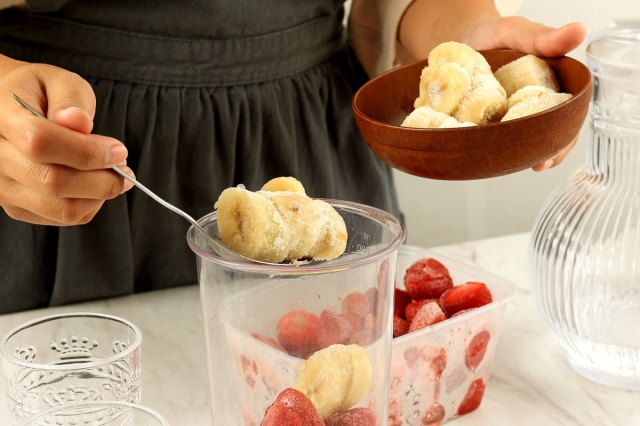 An image of a woman scooping frozen banana into a blender