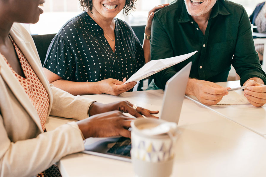 An image of a woman typing on a computer and talking to two people