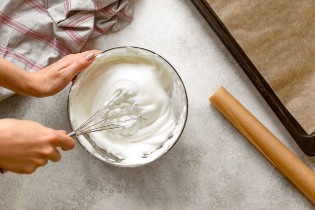 An image of a hand making whipped cream with a whisk in a bowl