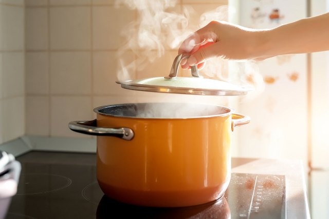 An image of a hand taking a lid off a boiling pot on the stove