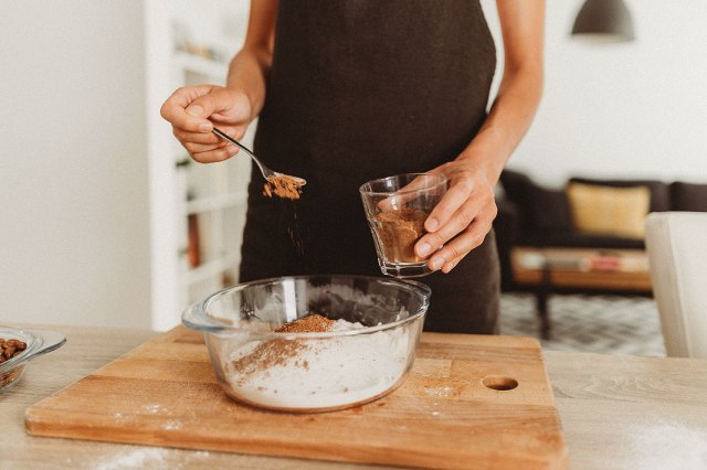 An image of a baker spooning cocoa powder into a bowl of dry ingredients
