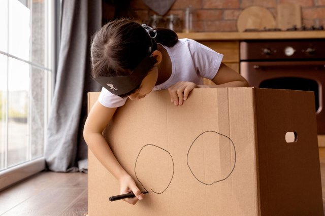 An image of a child drawing two big holes on a cardboard box