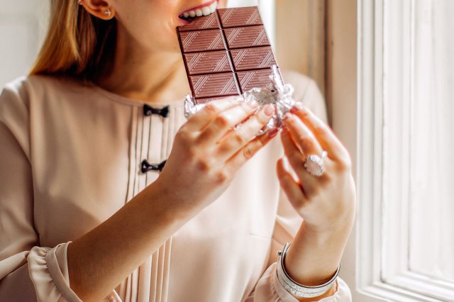 An image of a woman biting into a bar of chocolate