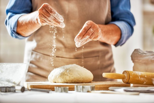 An image of a person sprinkling flour on bread dough