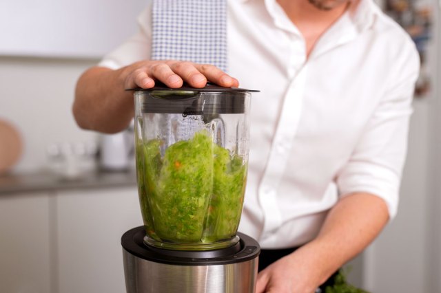 An image of a man making a green smoothie in blender.