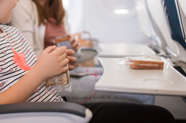 A child on an airplane holds a snack with their seat tray open in front of them