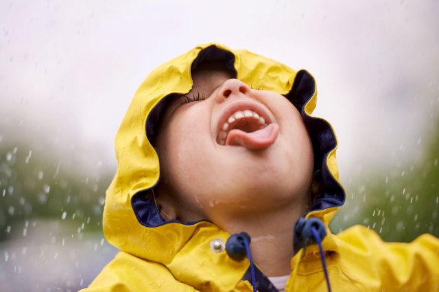 An image of a child in a yellow raincoat with his tongue out