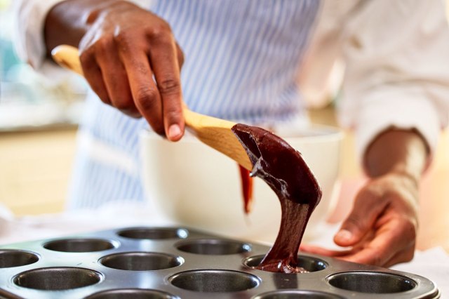 An image of a person pouring chocolate batter into a cupcake tin