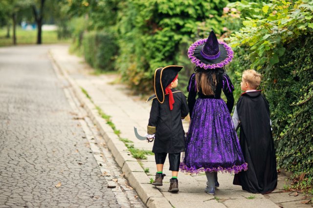 An image of three kids in Halloween costumes walking on the sidewalk