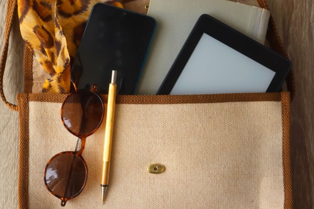 An image of a bag with a book, a tablet, a phone, a pen, glasses and a leopard pattern scarf.