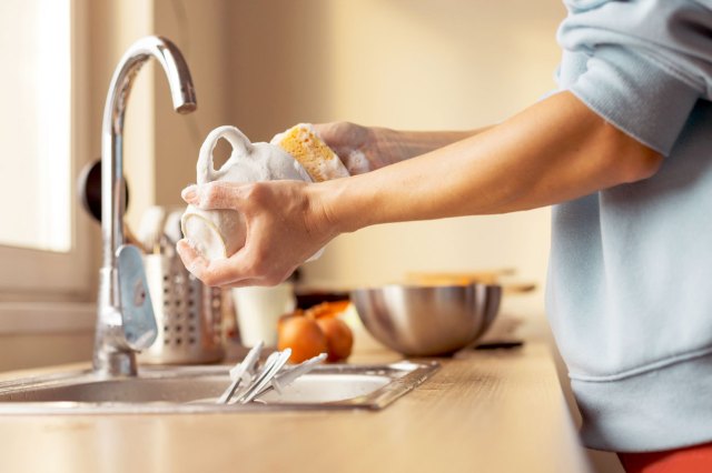 An image of a person washing a white coffee mug with a yellow sponge