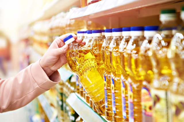 An image of a person taking a bottle of oil off a grocery store shelf
